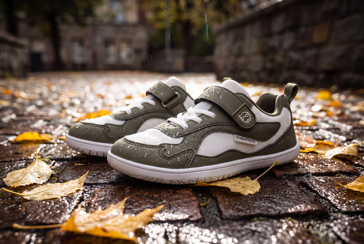 Everest Kids wasserabweisende Barfußschuhe auf nassem Kopfsteinpflaster mit Herbstlaub und Regentropfen